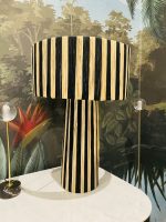 Black and natural raffia table lamp with vertical striped design, tall cylindrical base and wide handwoven drum lampshade.