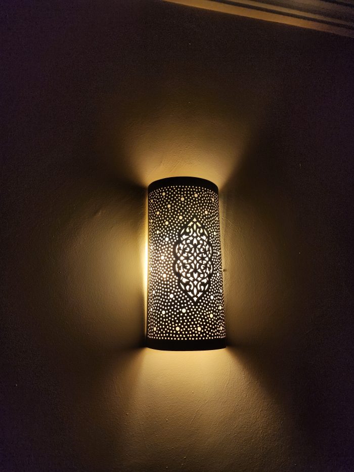 Handmade Moroccan pierced brass wall lamp with perforated pattern and warm up and down lighting.