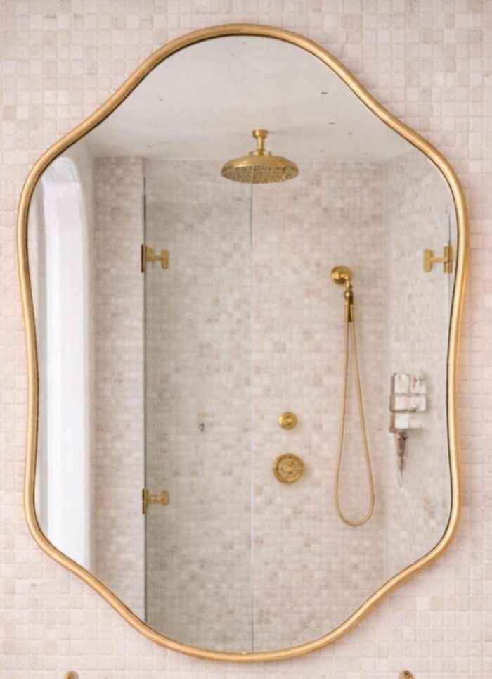 Handmade sculpted oval brass wall mirror with flowing curved edges and solid brass frame above double bathroom vanity.