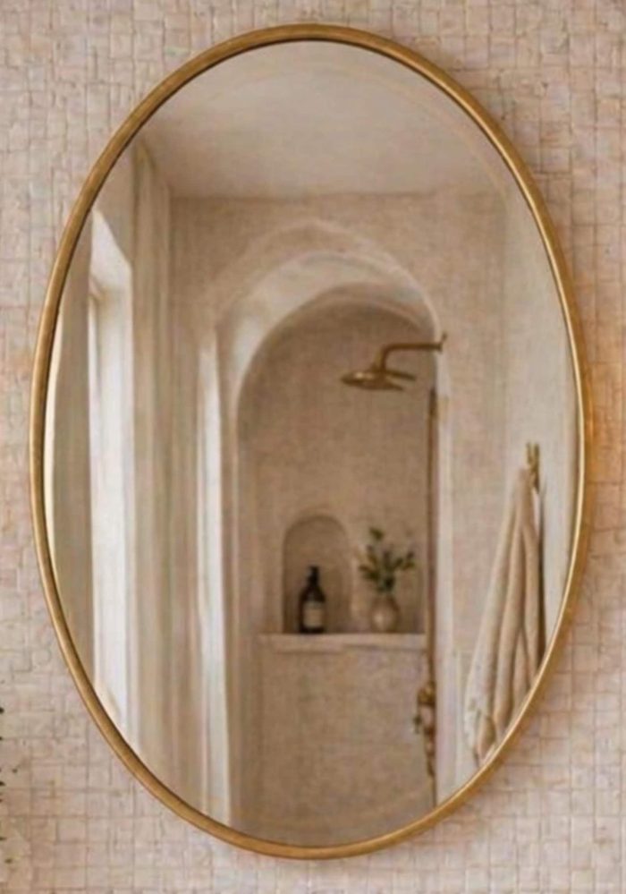 Oval brass bathroom mirror above vanity with brass fixtures and wall sconces