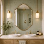 Handmade sculpted oval brass wall mirror with flowing curved edges and solid brass frame above double bathroom vanity.
