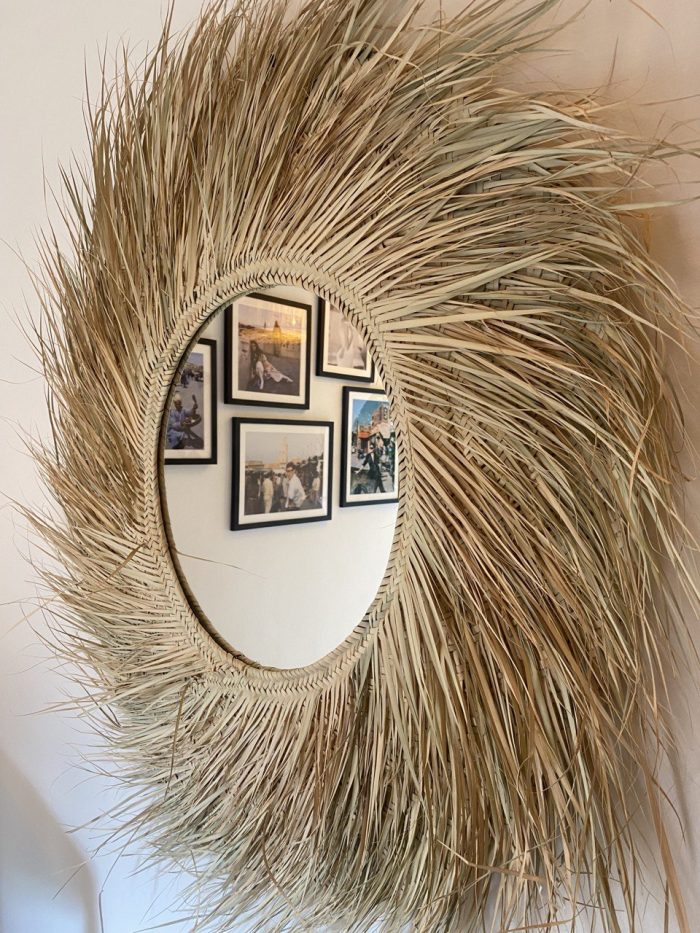 Handwoven palm leaf mirror with round glass center and natural sunburst fringe wall decor