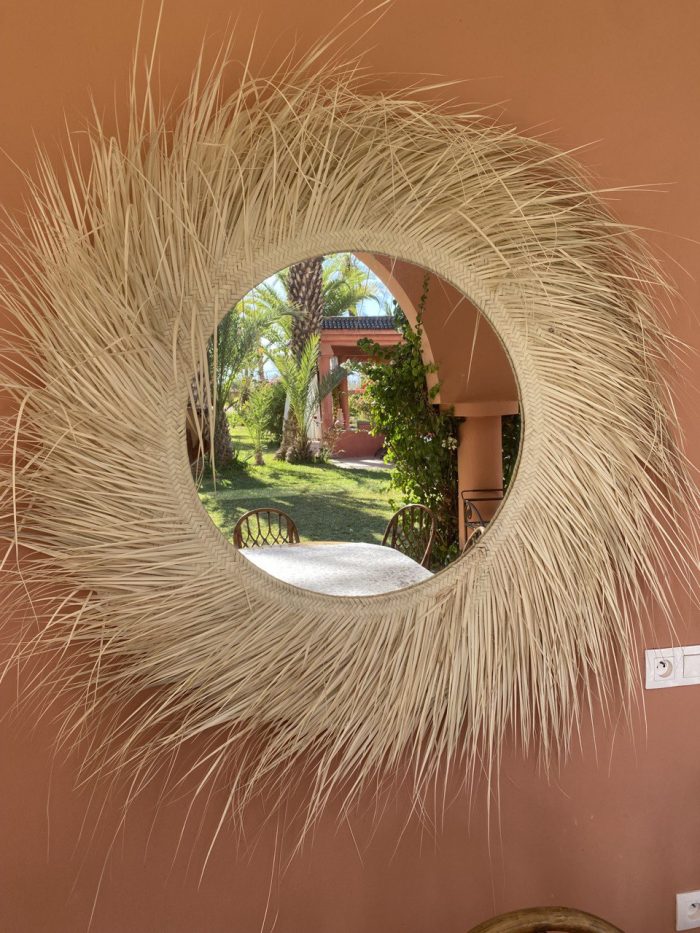 Handwoven palm leaf mirror with round glass center and natural sunburst fringe wall decor