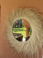 Handwoven palm leaf mirror with round glass center and natural sunburst fringe wall decor
